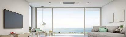 Modern living room with ocean views, a sofa, wall-mounted TV, and minimal decor. The Mitsubishi MLZ Indoor One Way Ceiling Cassette Air Handler delivers discreet, efficient air conditioning—ideal for low ceilings and comfort.