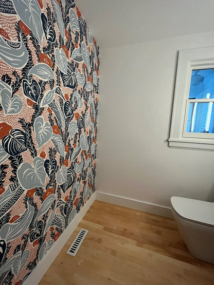 A room with a colorful patterned wallpapered wall, Madelyn Carter Steel Modern Chic Vent Covers in white on the wooden floor, a window, and part of a white toilet.