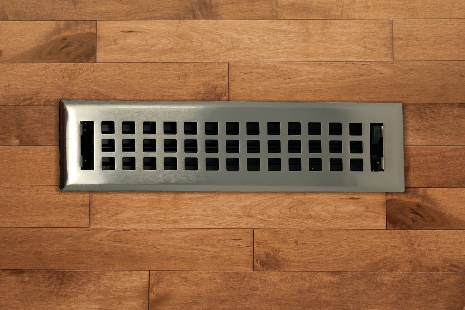 The Madelyn Carter Steel Artisan Vent Cover in Brushed Nickel features a grid pattern, installed in hardwood flooring to provide a stylish and durable finish.