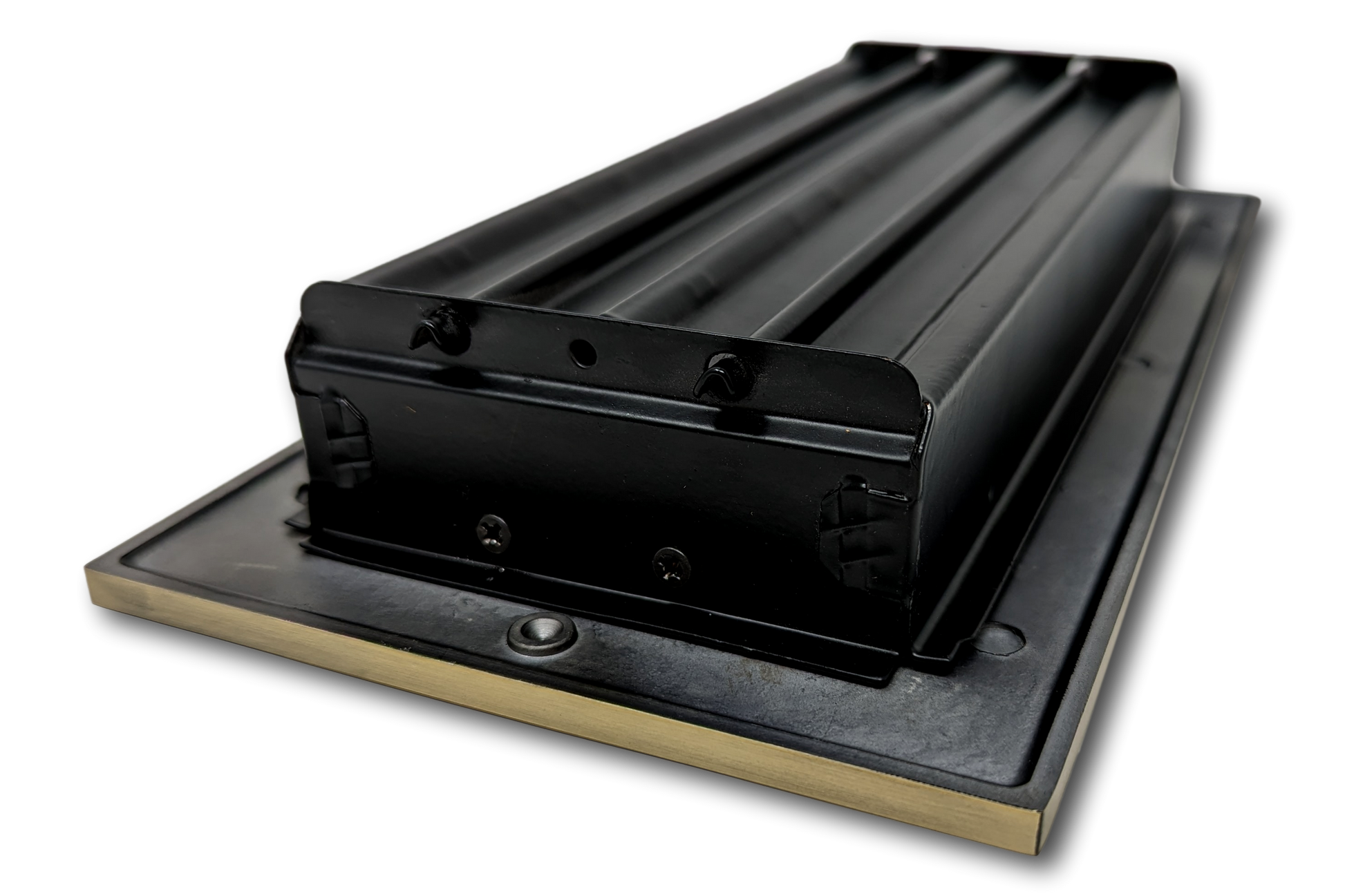 A close-up of Madelyn Carter's Cast Aluminum Linear Bar Vent Covers in Antique Brass, showcasing the black metal part on a rectangular base with a brass edge, photographed against a white background.