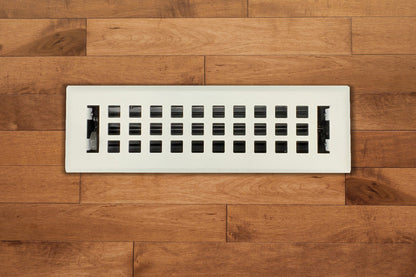 The Madelyn Carter Steel Artisan Vent Cover in white features a grid pattern and is installed in medium-toned wood flooring, adding a subtle modern touch to the space.
