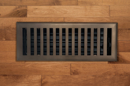 The Madelyn Carter Steel Modern Chic Vent Cover in oil rubbed bronze adds a stylish touch to light brown hardwood floors with its rectangular slats.