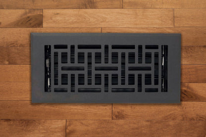 The Madelyn Carter Cast Aluminum Arts & Crafts Vent Cover in black, featuring a geometric design, is installed on a medium-brown wooden floor.
