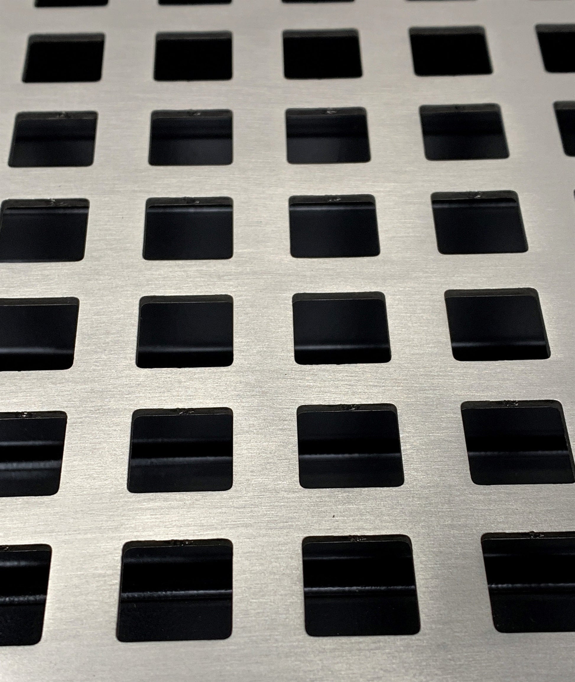A close-up of Madelyn Carter’s Steel Artisan Vent Covers in brushed nickel, showcasing evenly spaced square perforations in a grid pattern—ideal for ventilation or stylish décor.