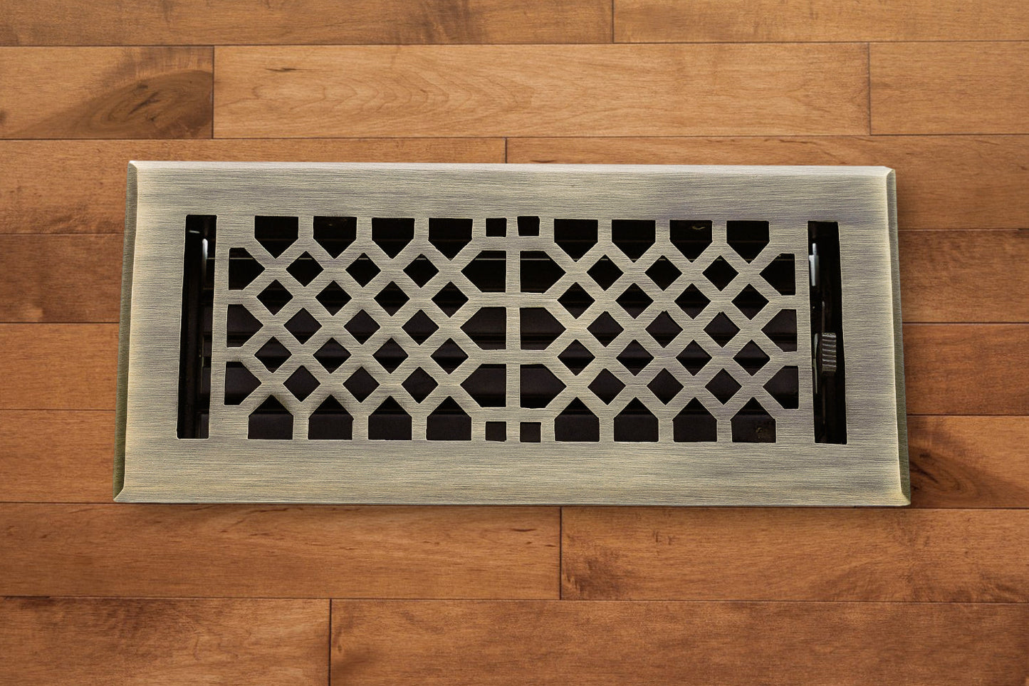 The Madelyn Carter Cast Brass Vintage Industrial Vent Cover in Antique Brass adds elegance to any wooden floor with its striking geometric pattern.