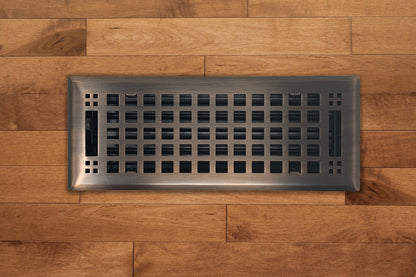 The Madelyn Carter Steel Artisan Vent Cover in Venetian Bronze features a grid pattern and is shown installed on light brown wood flooring.