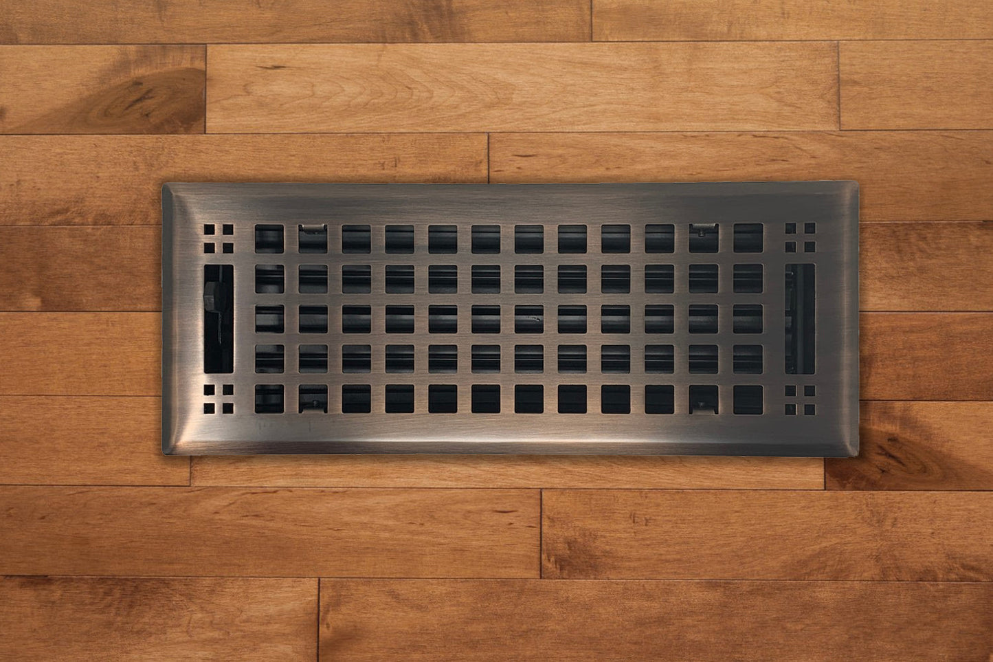 The Madelyn Carter Steel Artisan Vent Cover in Venetian Bronze features a grid pattern, seamlessly integrated into medium-toned wood floors for lasting durability and stylish appeal in your home.