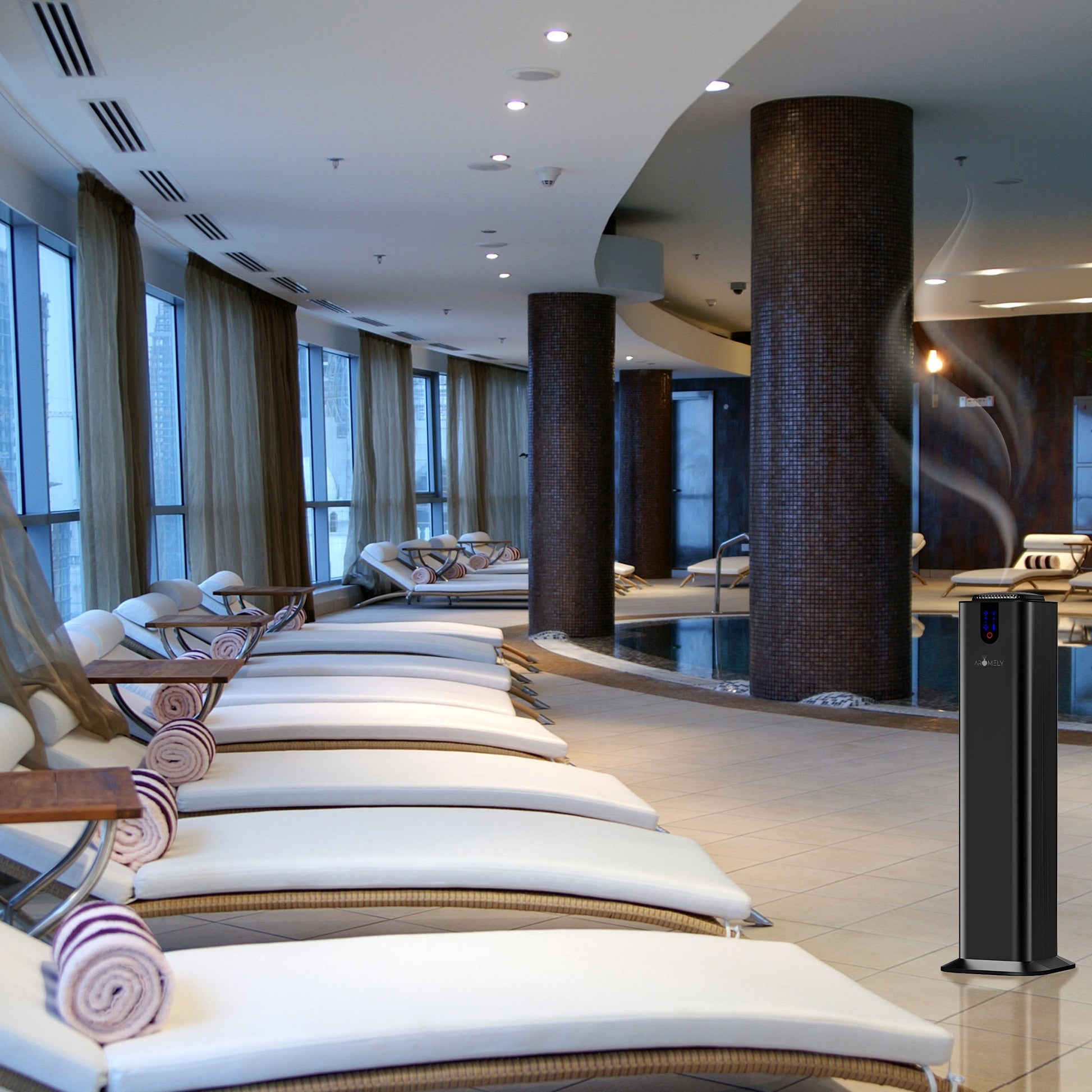 A modern indoor spa with lounge chairs, rolled towels, large windows, brown columns, a swimming pool, and the AROMELY Smart Bluetooth Scent Diffuser (up to 2,000 SQSF) by the seating area for maximum comfort.