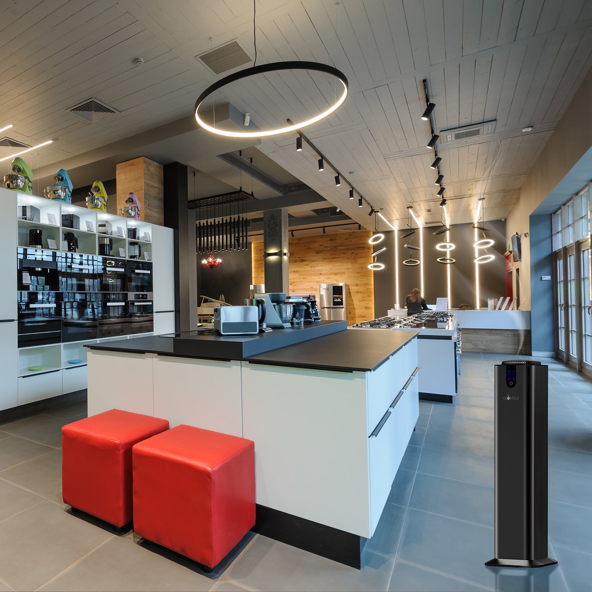 Modern kitchen with white cabinets, black countertops, red cushioned stools, hanging lights, appliances, and an Aromely Smart Bluetooth Scent Diffuser by AROMELY (covers up to 2,000 SQSF) featured in the foreground.