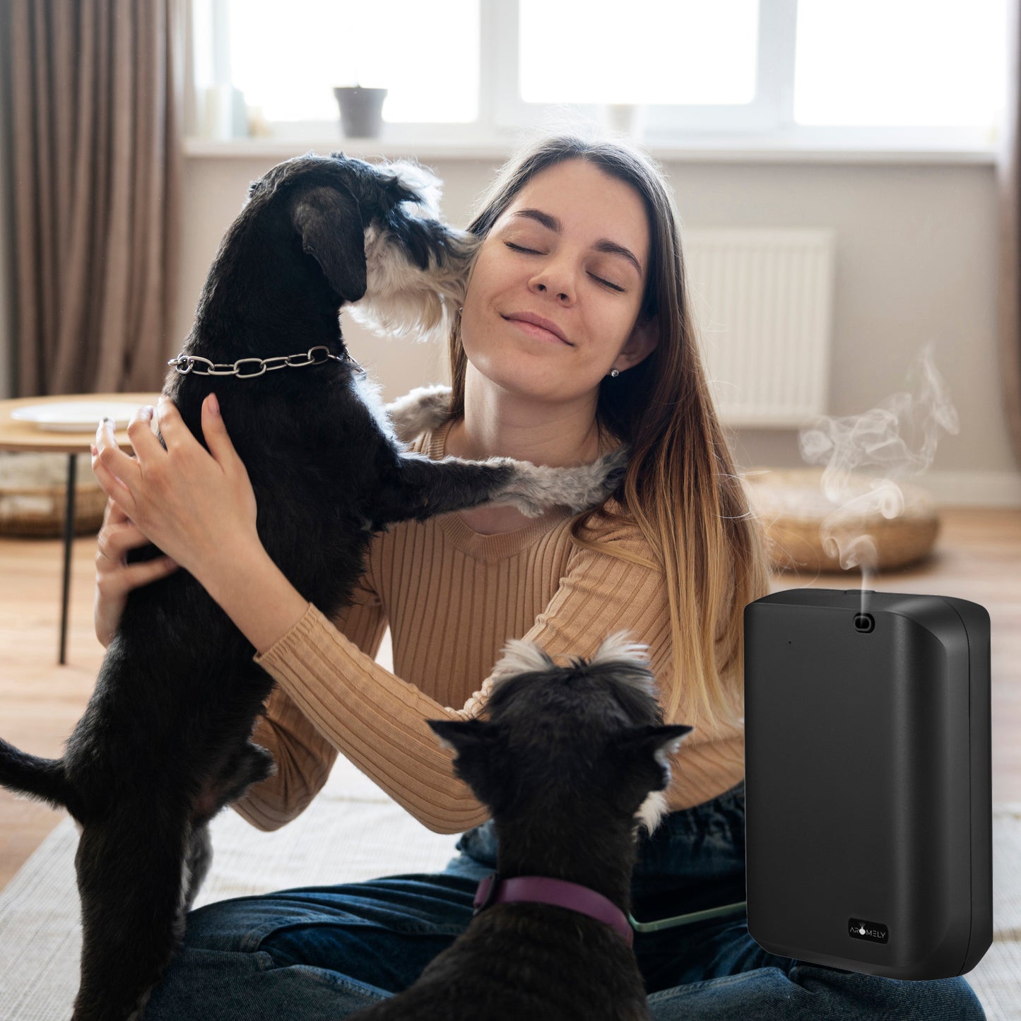 A woman sits indoors with two dogs, while the AROMELY Smart Scent Diffuser for Home, Office & SPA (covers up to 1,000 SQFT) gently emits a mist of essential oil nearby.