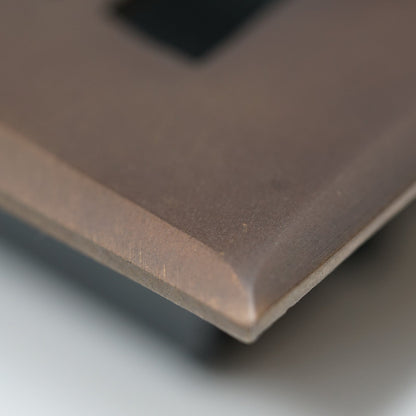 Close-up of a Madelyn Carter Cast Brass Baroque Vent Cover in Oil Rubbed Bronze, featuring its smooth, beveled edge and rectangular cutout against a softly blurred background.