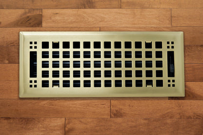 The Madelyn Carter Steel Artisan Vent Cover in brushed brass features a grid pattern, blending durability and style. Installed on a light brown wood floor, it adds elegance. The product description currently includes only CSS code.