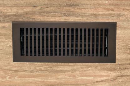 The Madelyn Carter Cast Brass Contemporary Vent Cover in oil rubbed bronze is installed in a wooden floor, offering a modern upgrade to traditional registers.