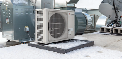 A Mitsubishi Outdoor Single Zone Standard Condenser (PUY, PUZ) sits on a snowy platform, built for efficient cooling-only performance in low ambient conditions, with other industrial equipment visible in the background.