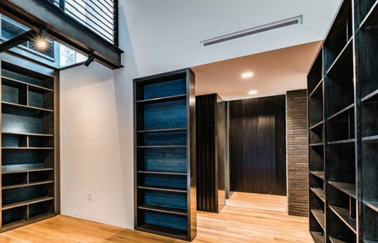 Modern interior space featuring dark built-in bookshelves, light wood flooring, white and black walls, ceiling lights, and a Mitsubishi Indoor Ceiling Concealed Air Handler - SEZ for customizable comfort with adjustable fan speed settings.